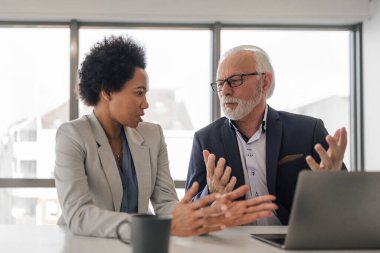 Confident business colleagues brainstorming while working on laptop. Male and female partners planning strategy during meeting. They are working at desk in the office.