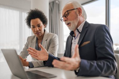 Confident male and female professionals brainstorming over laptop. Business executives discussing during meeting. They are sitting at desk while working in corporate office.