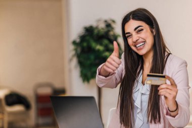 Smiling young woman, at the office, happy with the items she ordered online using credit card.