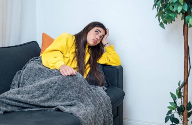 Düşünceli genç bir kadın, kanepesine uzanmış, tavana bakıyor, kolçaklarına yaslanıyor..