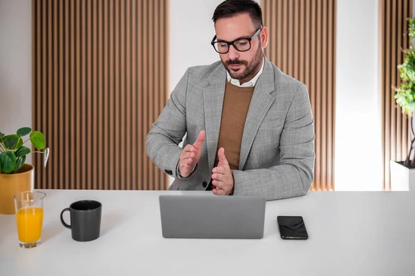 Hardworking entrepreneur in a suit, attending a meeting online, giving an explanation to his employees.