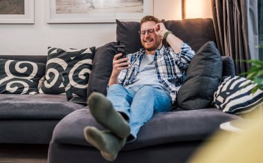 Sakin yetişkin bir adam, yatağında rahat ediyor, telefonundaki resim galerisine bakıyor..