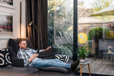 Sakallı sakallı rahat bir adam, cep telefonunu kullanıyor, internete giriyor, evde dinleniyor..