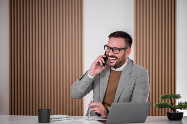 Neşeli girişimci ya da iş adamı, telefonuyla konuşuyor, ofisinde oturuyor..