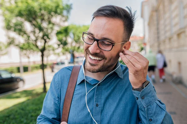 Calm young adult handsome man, putting earphones in both ears, making sure they fit, listening to music.