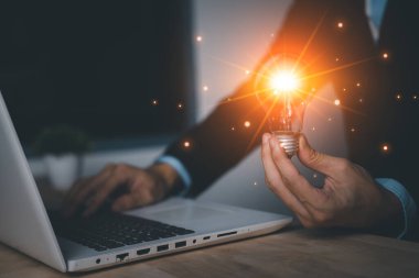İşadamı elinde laptop (dizüstü bilgisayar) ile sanal ampulü tutuyor. Yeni fikirler ilham ve yenilik teknolojisi konsepti. Bilim ve iletişim konsepti.