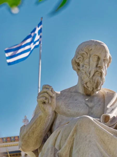 Plato marble statue and Greek flag through some tree folliage, Athens Greece