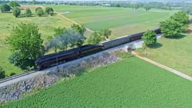 Ronks, Pennsylvania, Haziran 2021 - Güzel Bulutsuz Bir Bahar Günü 'nde Küçük Köprü Thru Ağaçları ve Çiftlik Bölgesi' nden Geçen Yolcu Koçlarıyla Bir Buharlı Motorun Buharlı Duman ve Buhar Buharlı Buhar Koçlarının Hava Görüntüsü