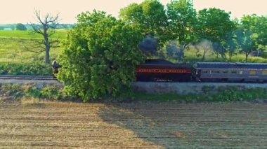 Ronks, Pensilvanya, Haziran 2021 - Yolcu Koçlarıyla Yolcu Treni Ağaçları ve Tarlaları Üzerinde Yolculuk Yapan Bir Buhar Motorunun Havadan Görünümü Altın Saat Güzel bir Öğleden Sonra Bahar Günü