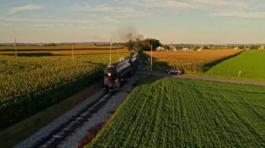 Bir Buhar Motoru Dumanı İçen ve Yolcu Koçlarıyla Güzel bir Öğleden Sonra Altın Saat Bahar Günü 'nde tek bir Track Thru Ağaçları ve Tarla Kırsalında Seyahat Eden Bir Buhar Manzarası