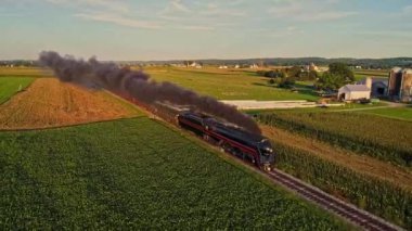 Bir Buhar Motoru Dumanı İçen ve Yolcu Koçlarıyla Güzel bir Öğleden Sonra Altın Saat Bahar Günü 'nde tek bir Track Thru Ağaçları ve Tarla Kırsalında Seyahat Eden Bir Buhar Manzarası