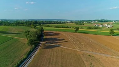 Güzel, güneşli bir günde, ekili tarlaları ve tek bir demiryolu hattının olduğu bir çiftlik manzarası.