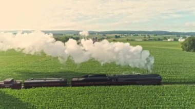 Ronks, Pennsylvania, July 2021 - Aerial View of an Antique Steam Engine and Passenger Coaches Traveling Along Countryside Blowing Smoke and Drone Traveling Parallel and Close To It, on a Sunny Summer Day