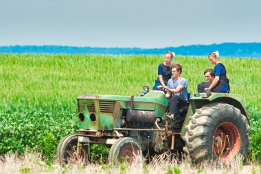 Amish Boy and Girl Teenagers Riding on a Old Tractor Thru Farmlands
