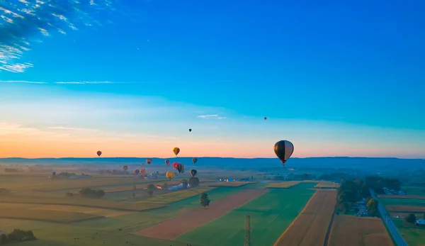 Vista aérea de muchos globos de aire caliente en vuelo a través de la campiña rural en una mañana temprana —  Fotos de Stock