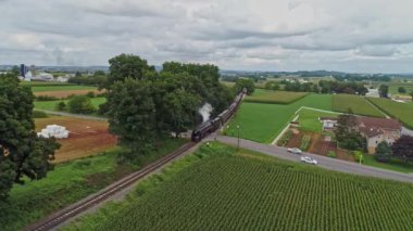 Ronks, Pennsylvania, 29 Ağustos 2021 - Antik Buharlı Yolcu Treni 'nin Önünde Bir Hava Görüşü Bulutlu Bir Yaz Günü' nde Bir Geçit ve Thru Zengin Tarım Alanlarında Duman Gidiyor