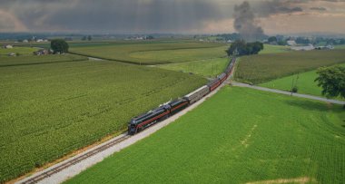 Drone View of an Antique Steam Engine, Approaching, Blowing Steam and Traveling Along the Countryside on a Sunny Day