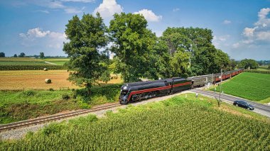 Drone View of an Antique Steam Engine, Approaching, Blowing Steam and Traveling Along the Countryside on a Sunny Day