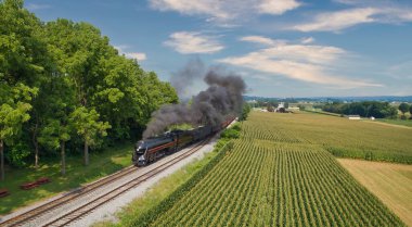 Drone View of an Antique Steam Engine, Approaching, Blowing Steam and Traveling Along the Countryside on a Sunny Day