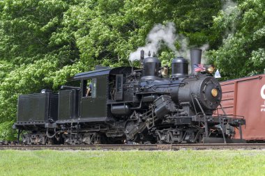 A View of a Antique Shay Steam Engine Moving Slowly Blowing Smoke and Steam on a Sunny Day