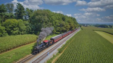 Ronks, Pennsylvania, August 29, 2021 - Drone View of an Antique Steam Engine, Approaching, Blowing Steam and Traveling Along the Countryside on a Sunny Day