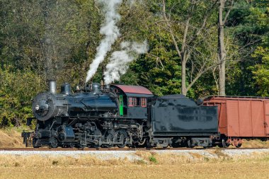 A View of a Steam Freight Train on a Single Track Going Thru Rural Countryside on a Sunny Day