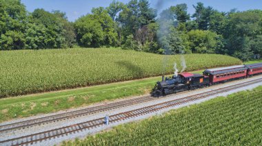 Ronks, Pennsylvania, August 28, 2021 - Drone View of an Antique Steam Engine, Approaching, Blowing Steam and With on Lookers Taking Photos on a Sunny Day
