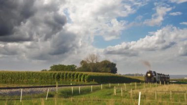 Steam Passenger Train Approaching Blowing Smoke and Steam Traveling Thru Corn Fields on a Sunny Day