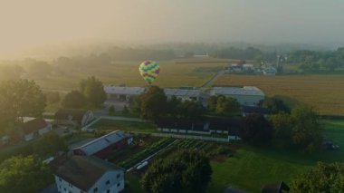 Drone View of a Single Hot Air Balloon Landing Near a Farm and Business in a Foggy Morning