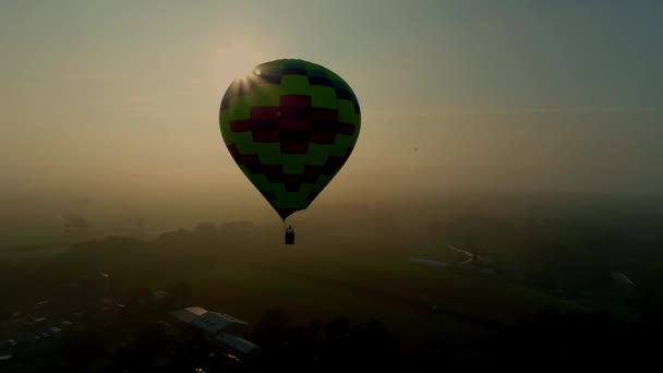 朝の霧の中で太陽によってシルエットによって浮かぶ単一の熱気球のドローンビュー — ストック動画