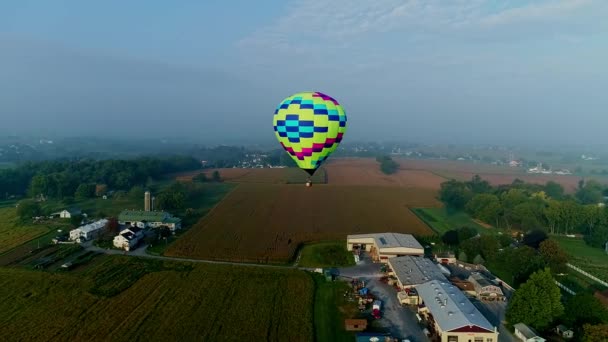 霧の朝に農場や企業が浮遊する単一の熱気球のドローンビュー — ストック動画