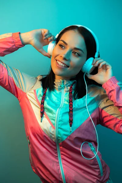 Hübsche junge Frau mit weißen Kopfhörern hört im Studio Musik im Neonlicht. — Stockfoto