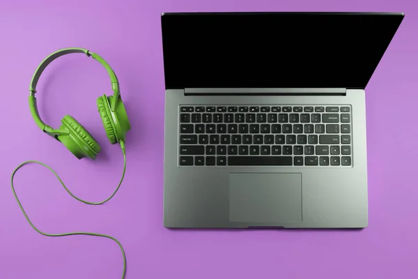 Photo de l'ordinateur moderne élégant ou portable et écouteurs verts sur fond violet. — Photo