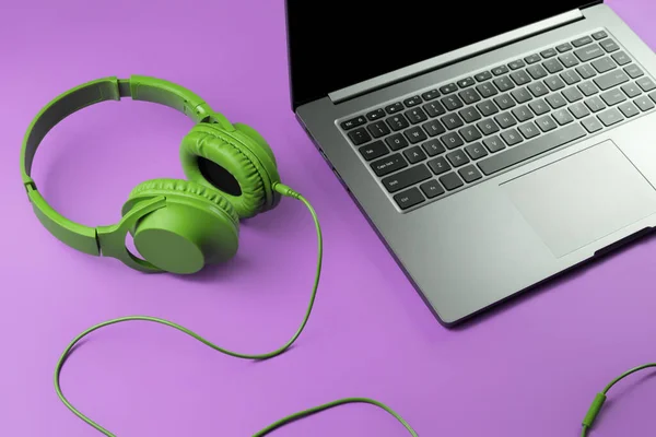 Ordinateur moderne ou ordinateur portable et écouteurs verts sur fond violet. — Photo