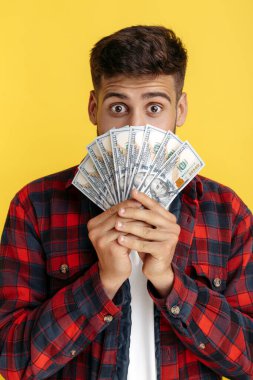 Şok olmuş sakallı hippi. Ekose gömlekli genç adam. Sarı arka plan üzerinden yüzünü nakit parayla kaplamış..
