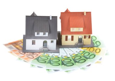 Miniature model of houses on stacked euro banknotes, on isolated white background. Real estate investment concept. Saving money for future retirement.