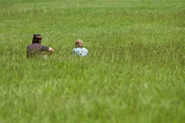 Man And Boy Sit In Grassy Meadow — Stock Photo, Image