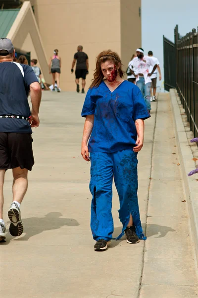 Female Zombie Nurse Skulks After Runners In 5K Run — Stock Photo, Image