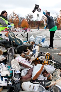 Volunteer Tosses Sneakers Into Shoe Pile At Recycling Event clipart