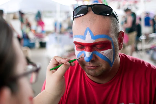 Człowiek staje się symbolem lafleur malowane na twarz na festiwalu — Zdjęcie stockowe