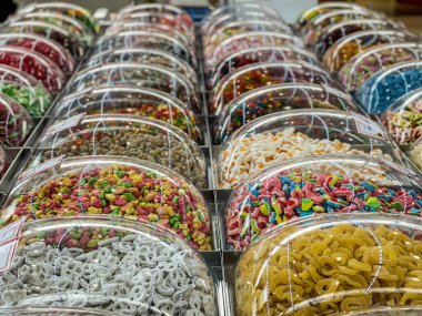 Rows of colorful, sugary sweets sit on display in plastic containers at mall food kiosk.