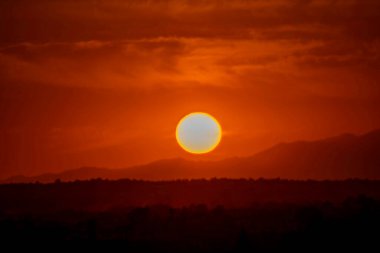 Kızıl güneş az bulutla dağların üzerinde batıyor.