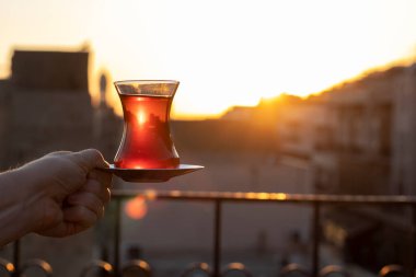 Günbatımında elinde bir bardak Türk çayı tutan kişi.