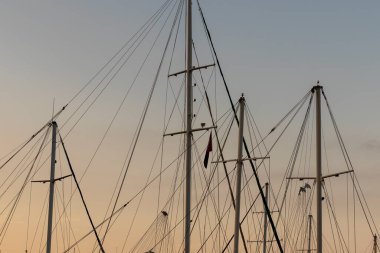 Yelkenli bir geminin direkleri ve ipleri. Gün batımında gökyüzü arka planında.