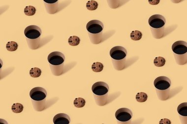 Kağıt bardakta sade kahve ve bej arka planda çikolata parçalı kurabiyeler. Kusursuz tekrarlama deseni.