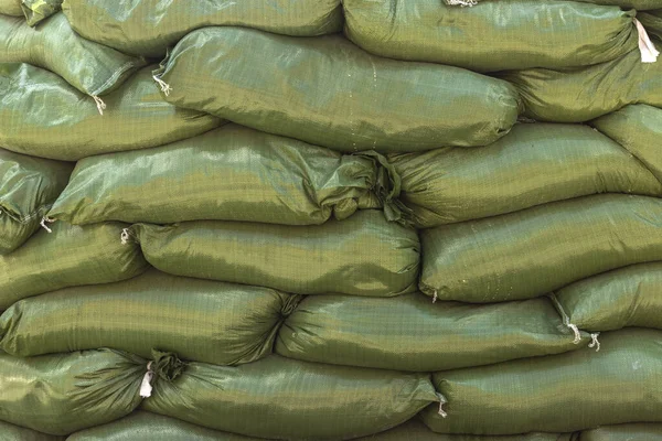 Protective sand bag barricade for military use. Background of many green sandbags for flood defense.