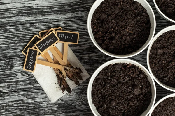 Metal çömleklere saksı toprağı ve aromatik bitkilerin isimlerinin yazılı olduğu tahta tabelalar. Ev kavramında yeşillik yetiştirme.