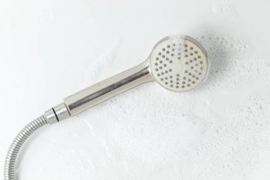 A shower head with foam is lying in the bathtub.