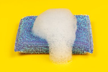 Blue cleaning sponge with foam on a yellow background.