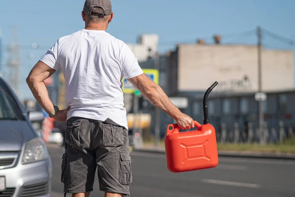 A red canister on the asphalt near the car. The car ran out of gas and stalled. A young man hoping for help on the road from other drivers. Stock Image